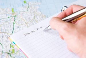 Hand writing travel plan in a lined spiral notepad arranged on a map